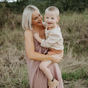 Jasmine is holding Weston in her arms on her hip and they are both smiling, standing in a field